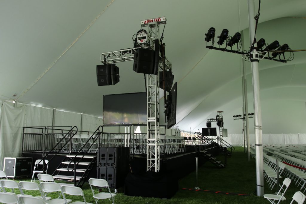 outdoor ceremony set up with staging and seating covered by a tent