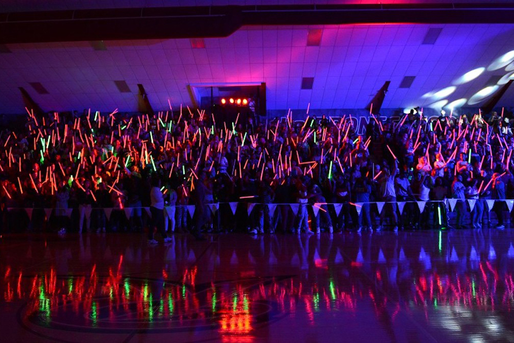 campus event in school gym. Bleachers filled with students waving LED glow tubes
